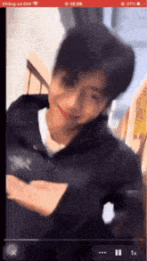 a man in a black jacket is smiling and looking at the camera on a cell phone screen .