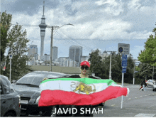 a person holding a flag with the name javid shah on the bottom right