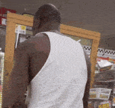 a man wearing a white tank top is standing in front of a display of super candy