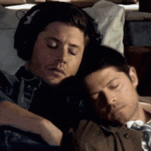 a man wearing headphones is hugging another man who is sleeping on a bed .