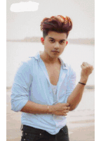 a young man wearing a white shirt and black jeans stands on a beach with his fist in the air