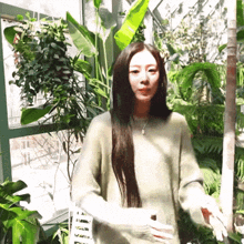 a woman in a green sweater is standing in front of plants