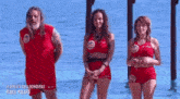 a man and two women in red swimsuits are standing in the water .