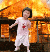 a little girl in front of a burning house wearing a pink shirt with a doll on it