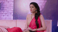 a woman in a red saree is sitting on a couch with a man laying on the floor .