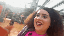 a woman with curly hair is smiling and wearing a pink shirt and a purple jacket