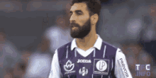 a man with a beard is wearing a purple and white joma jersey