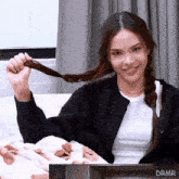 a woman is sitting on a couch holding her braided hair in front of a box that says drmr on it