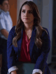a woman wearing a plaid jacket and a red shirt is sitting in a chair