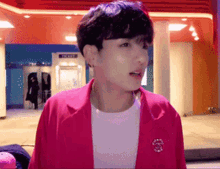 a young man wearing a pink jacket and a white shirt is standing in front of a telephone booth .