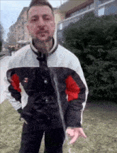 a man with a beard is standing in the grass with a hose coming out of his jacket ..