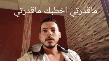 a man is standing in front of a brick wall with arabic writing on it