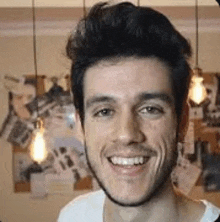 a young man with a beard is smiling in front of a wall with pictures on it .