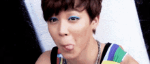a young woman wearing blue eye shadow is sticking her tongue out .
