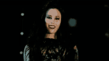 a woman with long black hair and red lipstick is standing in the dark .