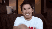 a man in a white shirt is smiling while sitting on a couch in a living room .