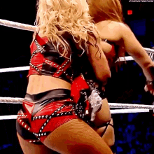 two women are wrestling in a ring and one of them is wearing a red top and black shorts .