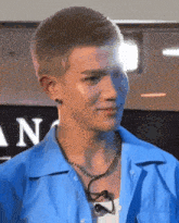 a young man wearing a blue shirt and a necklace is smiling .