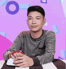 a young man in a striped shirt is sitting at a table holding a mouse .