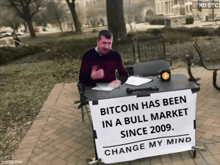 a man is sitting at a table with a sign that says bitcoin has been in a bull market since 2009