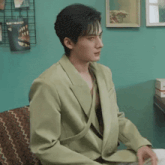a man in a green jacket is sitting on a couch looking at something .