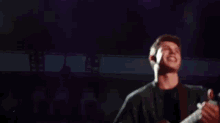 a man is playing a guitar on stage and singing into a microphone .