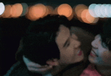 a man and a woman are kissing in front of a crowd of lights .