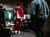 a man in a red jacket stands in front of a television with a man on the screen