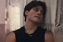 a young man leaning against a wall wearing a black tank top .