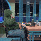 a man in a green hoodie is sitting at a table