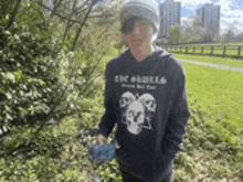 a young boy wearing a hoodie with a skull on it is standing in a park .