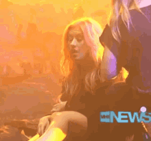 a woman with pink hair is sitting next to another woman in front of a screen that says news