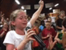 a little girl is singing into a microphone in front of a crowd .