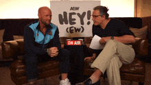 two men sit on a couch in front of a sign that says " hey "