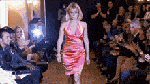 a woman in a pink dress is walking down the runway