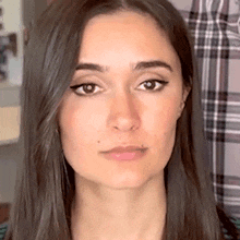 a close up of a woman 's face with plaid shirt in the background
