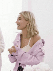 a woman wearing a purple jacket and a white tank top is smiling and laughing .