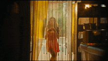 a woman in a red dress walks through a yellow curtain