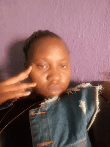 a woman wearing a denim vest is giving the peace sign