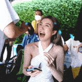 a woman in a white dress is laughing while holding a cell phone