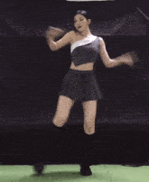 a woman in a pleated skirt is dancing in front of a black curtain .