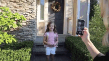 a woman taking a picture of a little girl in front of a house