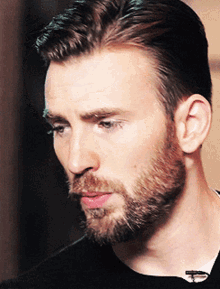 a close up of a man 's face with a beard wearing a black shirt