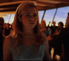 a woman wearing a pearl necklace stands in a crowd