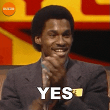 a man in a suit is smiling and clapping with the word yes behind him