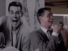 a man in a suit and tie is laughing in front of a picture of himself