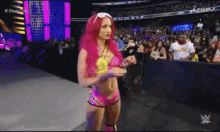 a woman with pink hair is standing in front of a crowd in a wrestling ring