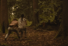 two people are fighting in the woods and one is laying on the ground
