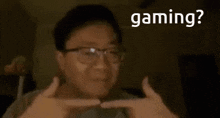a man wearing glasses is making a gun gesture with his hands and the words gaming behind him .