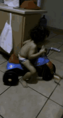 a child in a diaper is riding a toy motorcycle on a tiled floor